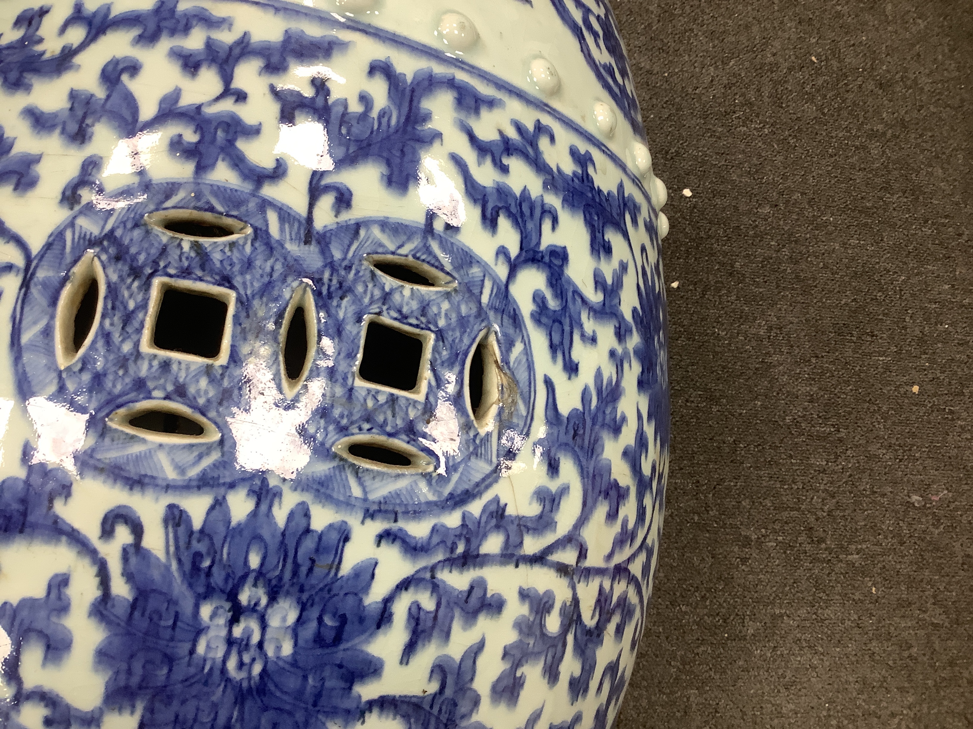 A Chinese blue and white porcelain stool, 19th century, painted with lotus flowers and scrolling foliage, pierced with coin motifs, between bands of raised bosses and foliate lappets, 48cm high